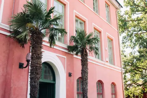 Hoby Kulle Herrgård i rosa nyanser med gröna fönster och palmer som ger en oväntad känsla.