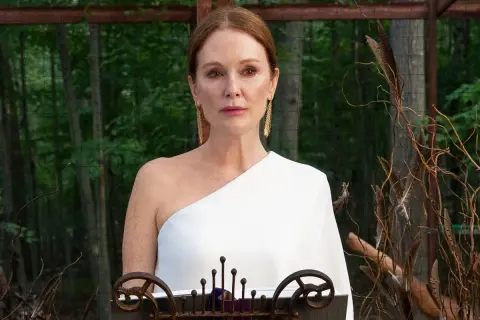 Julianne Moore i den vita klänningen i "Sirens"-serien, med en bakgrund av skog och dekorativa kvistar.