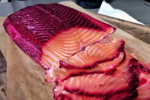 Rote Bete Lachs, mariniert und in Scheiben geschnitten, liegt auf Backpapier. Die leuchtend pinken Ränder des Lachses sind ein Blickfang.