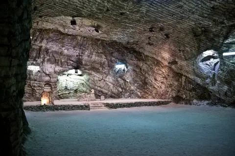 Interno della cattedrale di sale di Realmonte, con pareti rocciose stratificate e un altare illuminato.