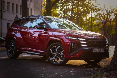 Czerwony Hyundai Tucson 4 w sportowej wersji N Line zaparkowany na tle jesiennych drzew i kamienicy.