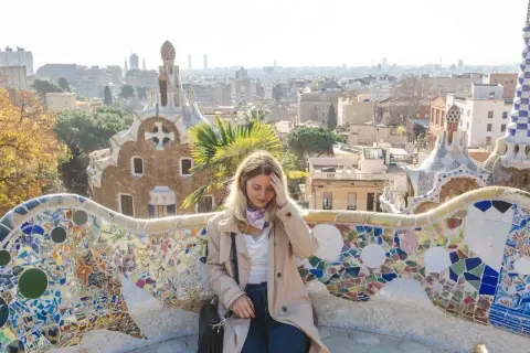 Frau sitzt auf einer bunten Mosaikbank im Park Güell, mit Blick auf Barcelona. Tolle Barcelona Tipps für deinen Besuch!