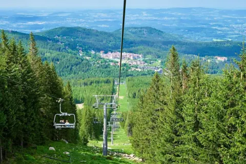 Wjazd kolejką linową na wysoką kopę szlak. Widok na zielone lasy i zabudowania w oddali.