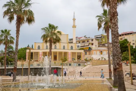 Fontanna i palmy przed meczetem w Durrës, Albania. Ludzie spacerują po placu.