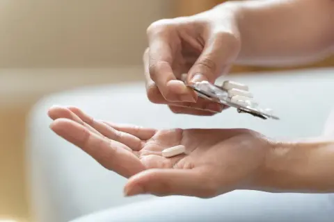 Eine Hand hält eine Tablette aus einer Blisterpackung, während eine andere Hand eine einzelne Tablette auffängt. Mögliche pregabalin nebenwirkungen im Blick.