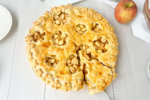 Goldbrauner Apfelkuchen mit Blätterteig-Dekor, ein Stück herausgeschnitten.