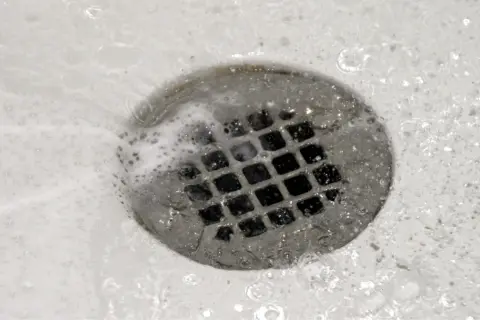 Acqua e schiuma scorrono nello scarico della doccia, un segno che il lavoro di pulire scarico doccia è stato fatto.