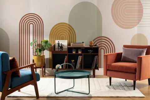 Salotto con poltrone colorate, mobile bar con giradischi e vinili, tavolino verde acqua e decorazioni murali in stile mid century.