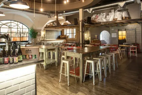 Interno del birrificio Legnano con tavoli, sgabelli e birre in bottiglia sul bancone.