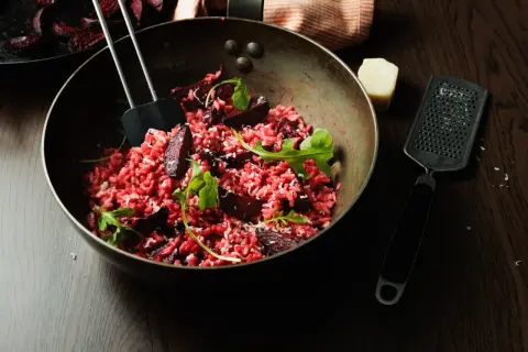 Un délicieux risotto betterave, garni de roquette fraîche et de copeaux de parmesan, prêt à être dégusté.