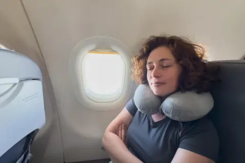 Frau schläft entspannt im Flugzeug mit Nackenkissen. Ein Beweis, warum man keine Angst vorm Fliegen haben muss.