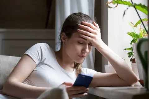 Zamyślona kobieta z ręką na czole, patrząca na telefon. Może to znak, po czym poznać, że ona chce odejść.