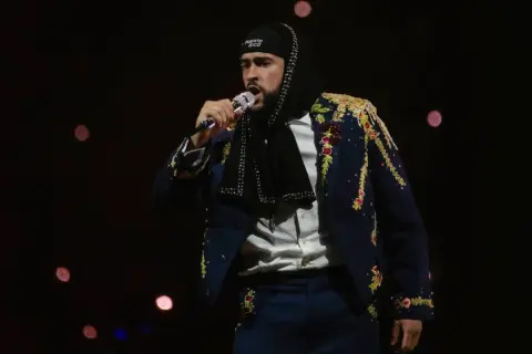 Bad Bunny koncert: artysta w ozdobnej marynarce i czapce z napisem "Puerto Rico" śpiewa do mikrofonu na tle rozmytych świateł.