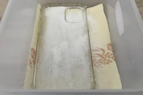 Przezroczyste etui na telefon zasypane sodą oczyszczoną, przygotowane do czyszczenia. To prosty sposób, jak wyczyścić zżółknięte etui.