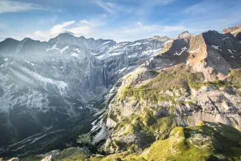 Le cirque de Gavarnie, majestueux amphithéâtre naturel, dévoile ses falaises abruptes, une cascade lointaine et des pentes verdoyantes sous un ciel bleu.