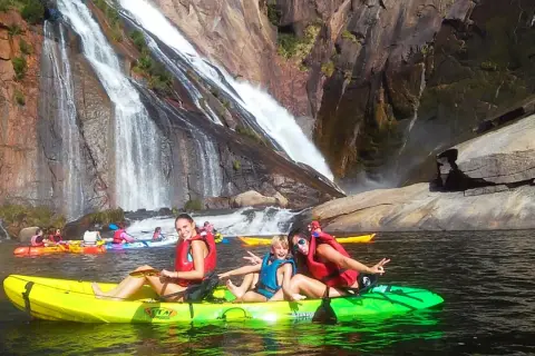 Familia disfrutando en kayak frente a la impresionante fervenza de Ézaro, con cascadas cayendo sobre rocas.
