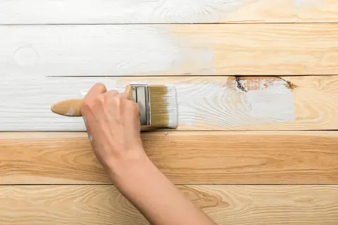 Metamorfoza starej boazerii w toku. Pędzel maluje białą farbą drewniane deski, odświeżając ich wygląd.