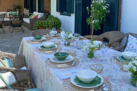Elegante decoracion mesa cocina al aire libre, con vajilla blanca y verde, flores y asientos de mimbre.
