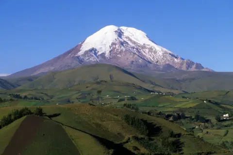 Ośnieżony wulkan Chimborazo, który jest najwyższą górą na świecie od środka Ziemi. W dole zielone wzgórza i pola.