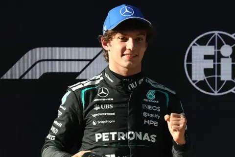 George Russell, piloto de Fórmula 1, celebra con un puño cerrado. Las noticias de Fórmula 1 lo muestran con el logo de Mercedes y FIA.