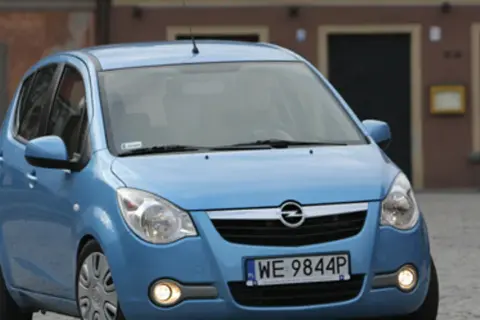 Niebieski Opel Agila 1.2 na brukowanej ulicy przed budynkiem.