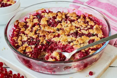 Ein leckerer Johannisbeer Crumble in einer Glasform, mit knuspriger Streuselhaube und saftiger roter Füllung.