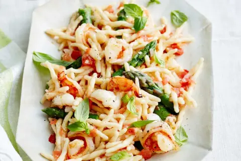 Trofie-Pasta mit Garnelen, Spargel und Tomaten, garniert mit Basilikum.