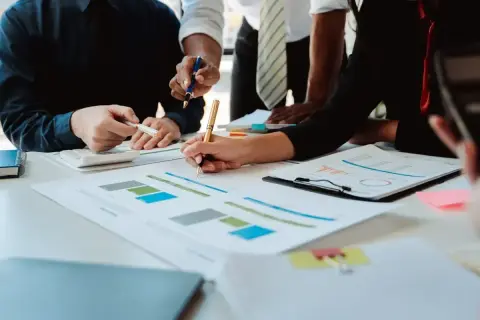 Zespół osób analizuje wykresy i dokumenty na stole, pracując nad finansami.