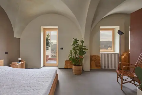Interno moderno con soffitti a volta, letto, pianta e vista panoramica. Sembra una di quelle case a un euro che diventano gioielli.