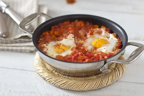 Un plat d'oeuf à la tomate mijoté dans une poêle, servi sur un dessous de plat en osier.