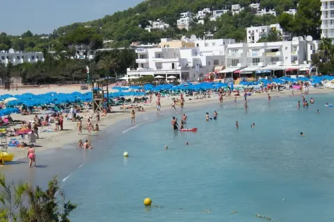 Lloret de Mar, lipiec: słoneczna pogoda zachęca do plażowania. Tłumy ludzi kąpią się i opalają na piaszczystej plaży, pod błękitnymi parasolami.