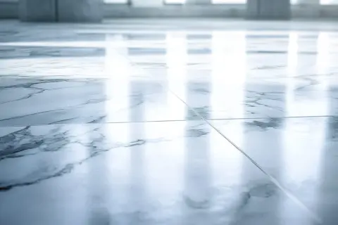 Suelo de mármol pulido con vetas grises. La luz se refleja intensamente, mostrando que el mármol es poroso y absorbe la humedad.