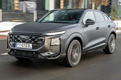 Nowe Audi Q3 w matowym, grafitowym kolorze sunie po drodze, prezentując swój sportowy charakter i nowoczesny design.