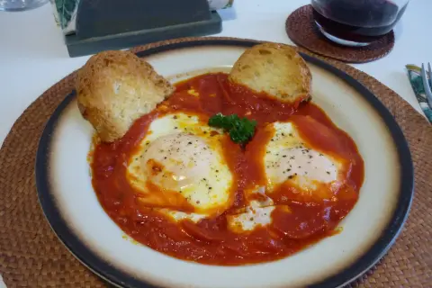 Uova in trippa marchigiana, un piatto saporito con uova cotte nel sugo di pomodoro, guarnito con pane tostato e prezzemolo.