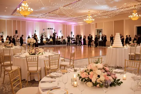 Elegancka sala weselna z oświetleniem, stołami i tortem.