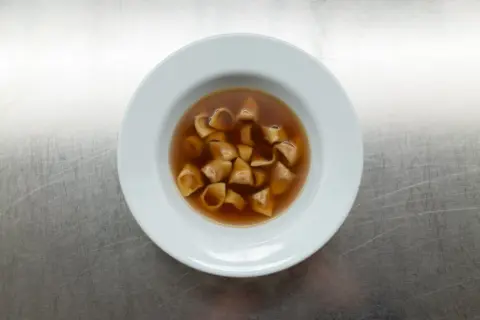 Eine Schüssel mit dampfendem Tortellini in Brodo auf einem metallischen Hintergrund.