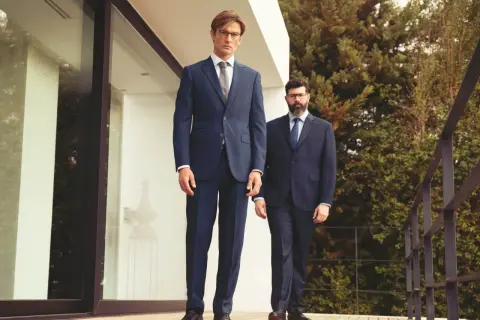 Zwei Männer in eleganten Anzügen, ein visueller anzug guide. Der vordere Mann trägt einen dunkelblauen Anzug, der hintere einen Nadelstreifenanzug.