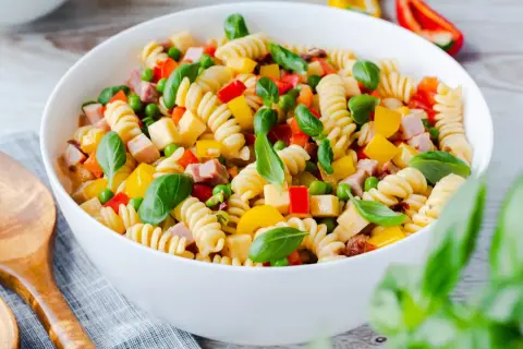Bunter Nudelsalat ohne Mayo mit Spiralnudeln, Erbsen, Paprika und Schinkenwürfeln, garniert mit Basilikum.