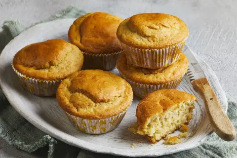 Goldbraune Buttermilch Muffins auf einem Holzteller, einer davon angebrochen, mit einem Messer daneben.