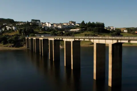 El puente de Portomarín cruza un embalse, con un pueblo en la colina al fondo.
