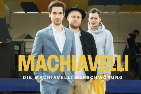 Drei Männer stehen vor einer Bühne, auf der "MACHIAVELLI" steht. Sie sind die Macher des Machiavelli Podcast.