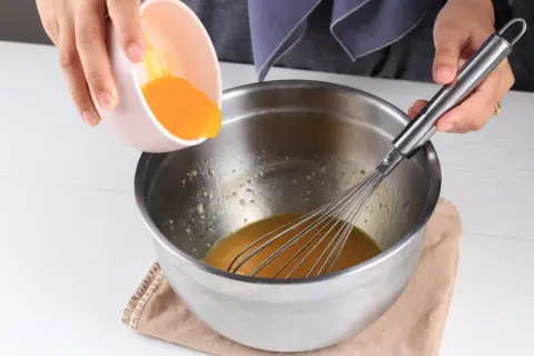 Dodawanie żółtka do miski z ubijaczką, przygotowanie do pysznego deseru kogel mogel.