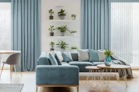 Przytulny salon w stylu marynistycznym. Jasne zasłony, wygodna kanapa i rośliny tworzą relaksującą atmosferę.