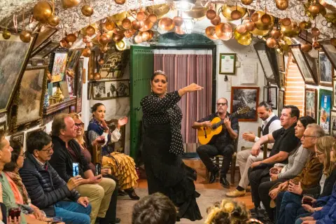 Una bailaora de flamenco, con un guitarrista y público, en un local decorado con cobre. ¡Gracias en flamenco!