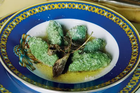Strangolapreti alla trentina, verdi e saporiti, serviti in un piatto elegante con burro fuso e salvia croccante.