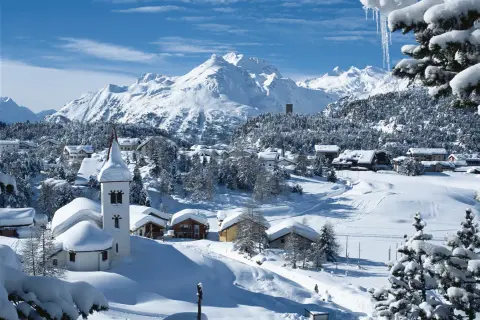 Winteridylle in der Schweiz: verschneite Berge, ein Dorf mit Kirche und Häusern, umgeben von Tannen.