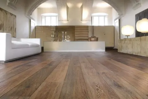 Acuchillado de parquet de madera rústica en un salón moderno con sofá blanco y lámparas.