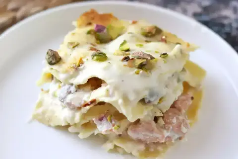 Porzione di lasagne bianche sfiziose con pistacchi e un ripieno cremoso, servite su un piatto bianco.