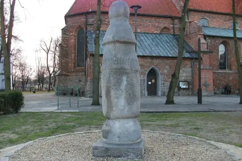 Kamienny słup milowy z inskrypcją przed ceglanym kościołem.