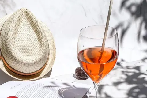 Ein Aperol Spritz im Glas neben einem Strohhut und einem Buch.